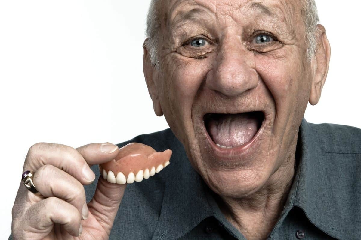 Senior man happily holding new dentures, demonstrating successful denture adjustment and fit.