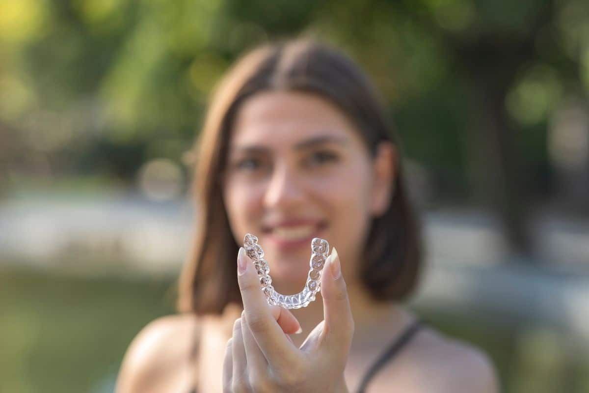Woman holding clear Invisalign aligner showing transparent orthodontic treatment option.