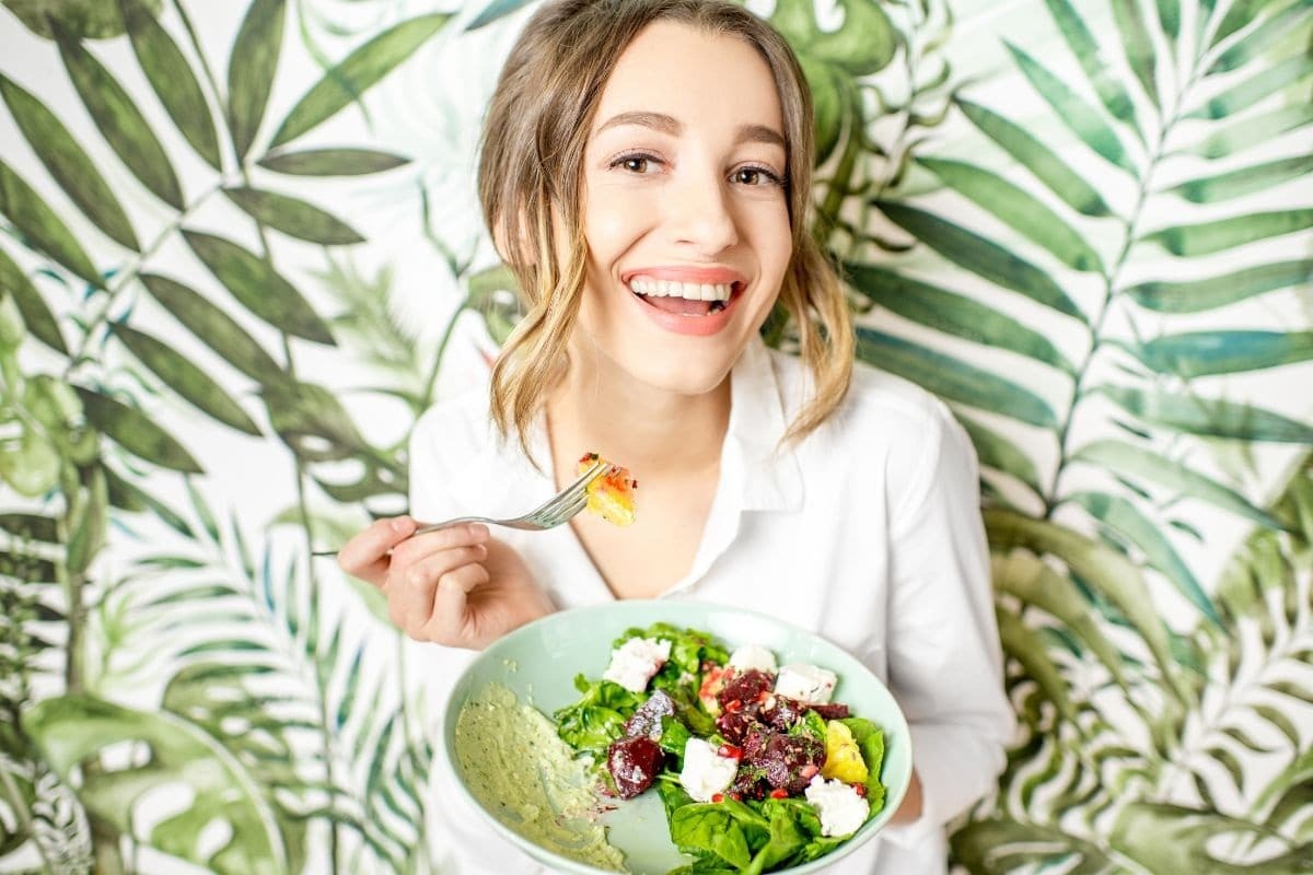 Happy woman eating a colorful salad with greens and white cheese after teeth whitening treatment.