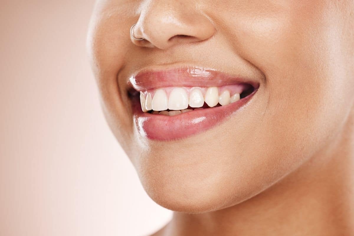 Woman with bright white teeth and healthy gums smiling against a neutral background.